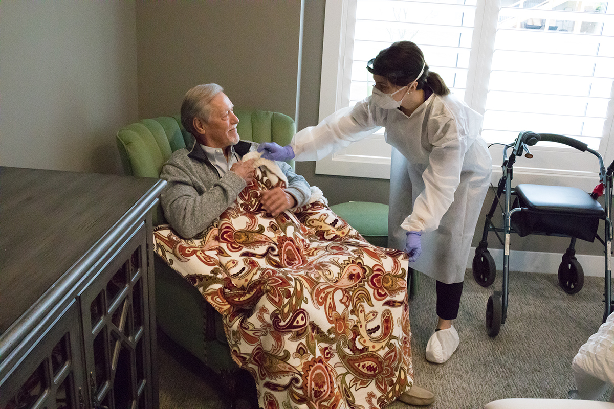 Caregiver wearing PPE helping senior