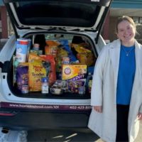 Lady standing with pile of donations in the back of car