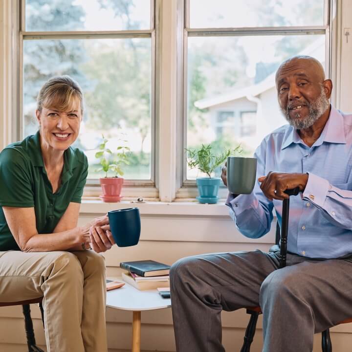 A Home Instead caregiver and an elderly man enjoy coffee together on a porch, showcasing shared moments of relaxation and connection.