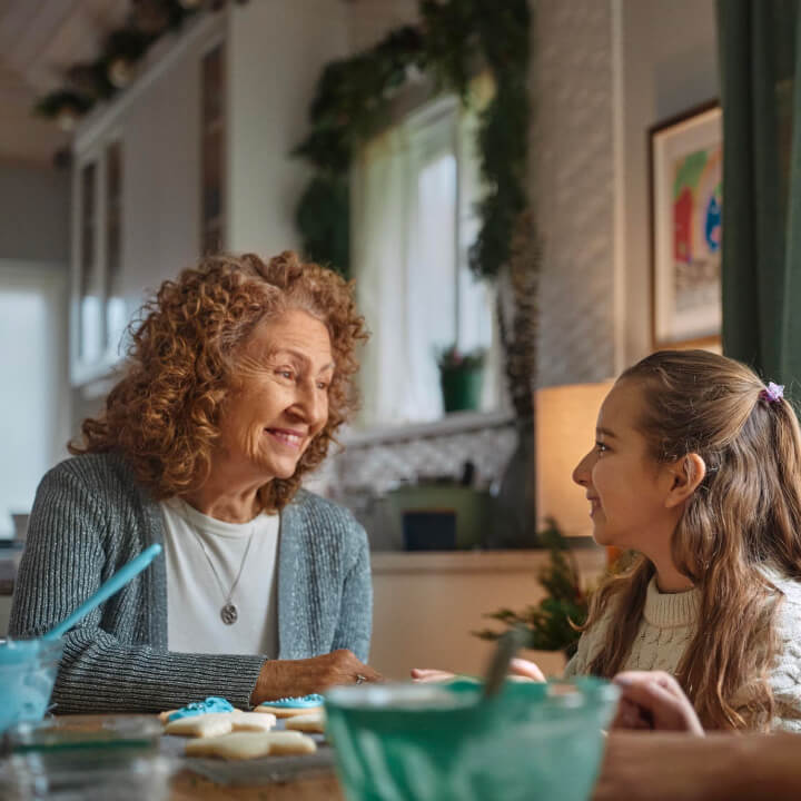 An elderly woman and a young girl baking cookies together at a kitchen table, symbolizing joy, connection, and family moments.