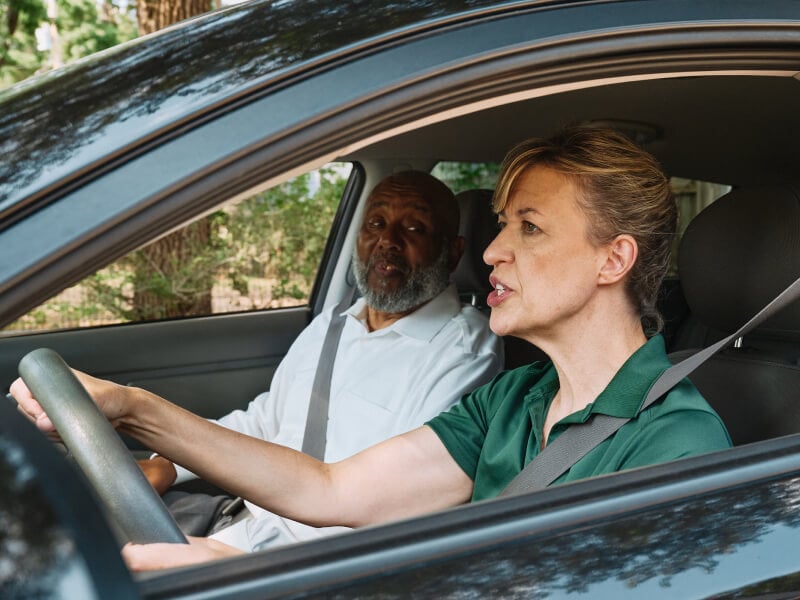 A Home Instead caregiver assists an elderly man in the passenger seat of a car, preparing for a safe and comfortable ride, showcasing reliable transportation support.