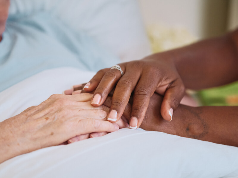 A close-up of a Home Instead caregiver's hands gently holding the hands of an older adult, showcasing compassion, trust, and care.